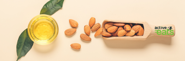 Image showing almonds in a wooden spoon and almond oil next to it in an open glass jar.