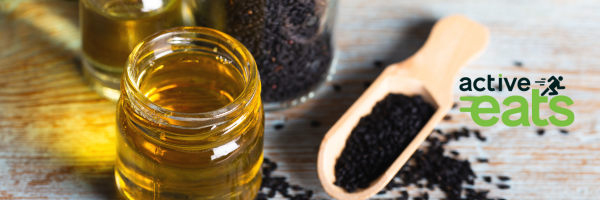 Image showing black seeds in a wooden spoon and black seed oil in a open jar next to it.